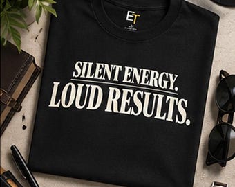 Può includere: Una t-shirt nera a maniche corte con la scritta bianca SILENT ENERGY. LOUD RESULTS. stampata sul petto. La maglietta presenta un girocollo e un piccolo logo ET sul colletto interno. Sotto la maglietta è visibile il testo DISCIPLINE CREATES FREEDOM.
