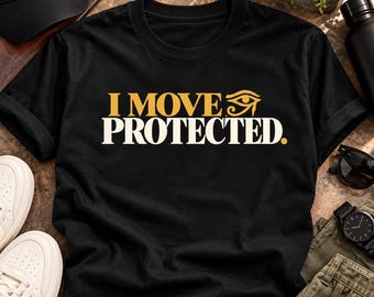 Può includere: Una t-shirt nera a maniche corte con la scritta "I MOVE" in lettere dorate seguita da un simbolo dell'Occhio di Horus, con la parola "PROTECTED." stampata in grandi lettere maiuscole bianche sulla parte anteriore del capo.
