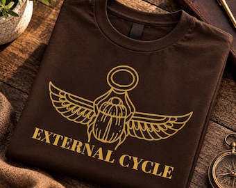 Può includere: Una t-shirt a girocollo marrone scuro con una grafica color oro raffigurante uno scarabeo alato, posizionata sopra il testo "EXTERNAL CYCLE" in un carattere grassetto maiuscolo. Il design è stampato con uno stile a linee pulite.