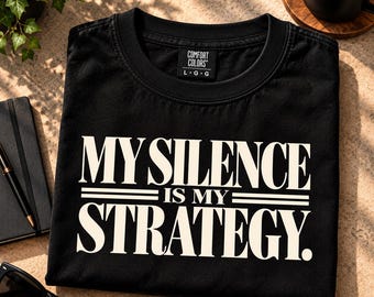 Può includere: Una t-shirt nera a maniche corte con scollo rotondo ed etichetta del marchio Comfort Colors. La maglia presenta il testo stampato in bianco MY SILENCE IS MY STRATEGY in un carattere grassetto maiuscolo, accentuato da due linee orizzontali.