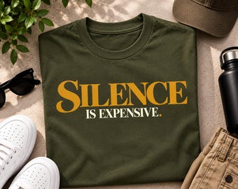 Può includere: Una t-shirt a maniche corte color verde oliva con la scritta SILENCE in grandi lettere dorate e IS EXPENSIVE in lettere bianche più piccole con un punto dorato. La maglietta è distesa, presenta un girocollo e una texture in cotone.