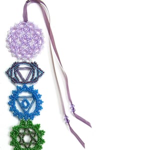 May include: A beaded chakra bookmark or hanger with a purple ribbon. The bookmark features seven chakras, each represented by a different colour and symbol. The chakras are arranged in a vertical line, starting with the crown chakra at the top and ending with the root chakra at the bottom. The text "Chakra Bookmark or Hanger" and "design by Sandra D Halpenny" is printed below the chakras.