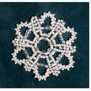 Puede incluir: Un patrón de adorno de copo de nieve de cuentas blancas, con instrucciones para el tamaño y la cantidad de cuentas. El patrón es para un copo de nieve de 3,8 cm.