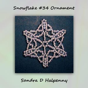 Puede incluir: Un adorno de copo de nieve de cuentas de color morado claro, sobre un fondo negro. El copo de nieve es una estrella de seis puntas con un diseño delicado. El texto "Snowflake #34 Ornament" está en la parte superior de la imagen y "Sandra D Halpenny" en la parte inferior.