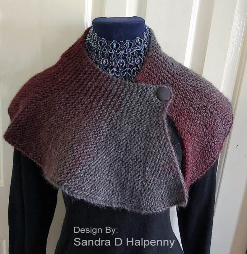 Peut inclure: Un col roul&eacute; en tricot gris et bordeaux avec une fermeture &agrave; bouton unique. Le col est drap&eacute; sur un mannequin portant une chemise noire et un collier de perles. Le texte "Design By: Sandra D Halpenny" est en bas de l'image.