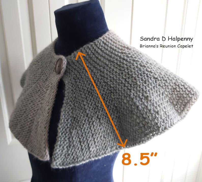 Peut inclure: Un capuchon en tricot gris et beige avec une fermeture &agrave; bouton. Le capuchon mesure 8,5 pouces de large. "Sandra D Halpenny Brianna's Reunion Capelet" est &eacute;crit sur l'image.