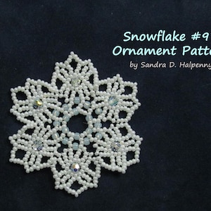 Puede incluir: Un patrón de adorno de copo de nieve de cuentas blancas, con el título "Snowflake #97 Ornament Pattern by Sandra D. Halpenny".