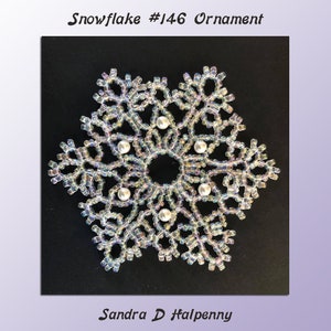Puede incluir: Un adorno de copo de nieve blanco hecho de cuentas iridiscentes con acentos de perlas blancas. El copo de nieve está sobre un fondo negro. El texto "Snowflake #146 Ornament" está sobre el copo de nieve y el texto "Sandra D Halpenny" está debajo del copo de nieve.