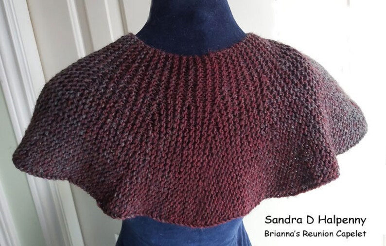 Peut inclure: Un capuchon en tricot bordeaux et gris avec un bord festonn&eacute;. Le capuchon est pr&eacute;sent&eacute; sur un mannequin. Le texte "Sandra D Halpenny Brianna's Reunion Capelet" est visible en bas de l'image.