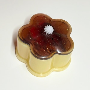 Op de afbeelding: Een bloemvormige sieradendoos met een doorschijnend bruin deksel en een lichtgele basis. De bovenkant heeft een donkerbruine, glinsterende laag met een witte werveling in het midden. Een uniek decoratief item.