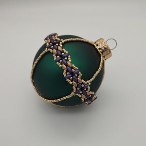 May include: A green glass Christmas ornament with a gold and purple beaded trim.