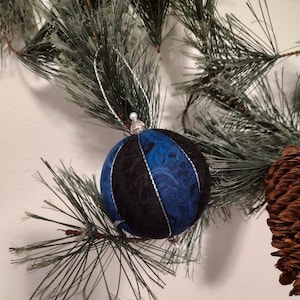 May include: A blue and black fabric Christmas ornament with a silver top and a silver string.