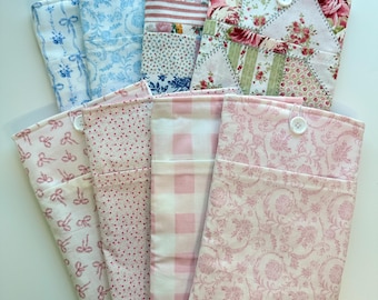 May include: A collection of fabric pouches in various patterns and colors. Designs include floral, polka dots, bows, and gingham. Some pouches have button closures. The color palette is primarily pastel pinks, blues, and whites.