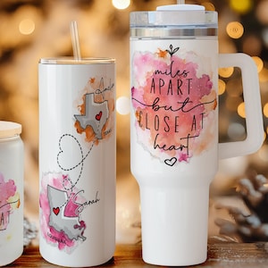Pu&ograve; includere: Una collezione di bicchieri bianchi con contorni di stati con cuori e la scritta "miles apart but close at heart". Include una tazza, un bicchiere, un bicchiere e un bicchiere da viaggio. Le stoviglie sono decorate con accenti acquerellati rosa e arancioni.