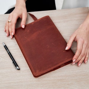May include: A brown leather bound journal with a simple design. The journal is closed and lying flat on a wooden surface.