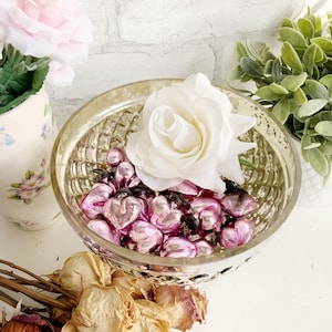 Peut inclure: Un bol en verre à bordure dorée rempli de cœurs en verre rose, une rose blanche et un fond floral.