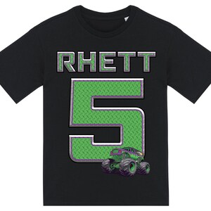 Może przedstawiać: Czarny t-shirt z napisem "RHETT" w srebrnych i zielonych literach blokowych. Duża zielona cyfra "5" jest wyśrodkowana na koszulce, z wzorem w romby. Grafika monster trucka znajduje się na dole.