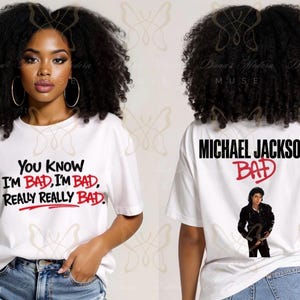 May include: White t-shirt featuring the text "You Know I'm Bad, I'm Bad, Really Really Bad" in black and red. The back of the shirt displays "Michael Jackson Bad" with an image of Michael Jackson. The shirt is worn by a person.