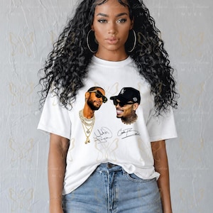 May include: A white short-sleeve t-shirt featuring a graphic print of two men wearing sunglasses and jewelry, accompanied by two handwritten-style signatures. The shirt is paired with light blue denim jeans that have distressed knee detailing.