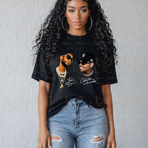 May include: A black short-sleeve t-shirt featuring a graphic print of two men wearing sunglasses and chains, accompanied by their signatures. The shirt is paired with light blue distressed denim jeans that have rips at the knees.
