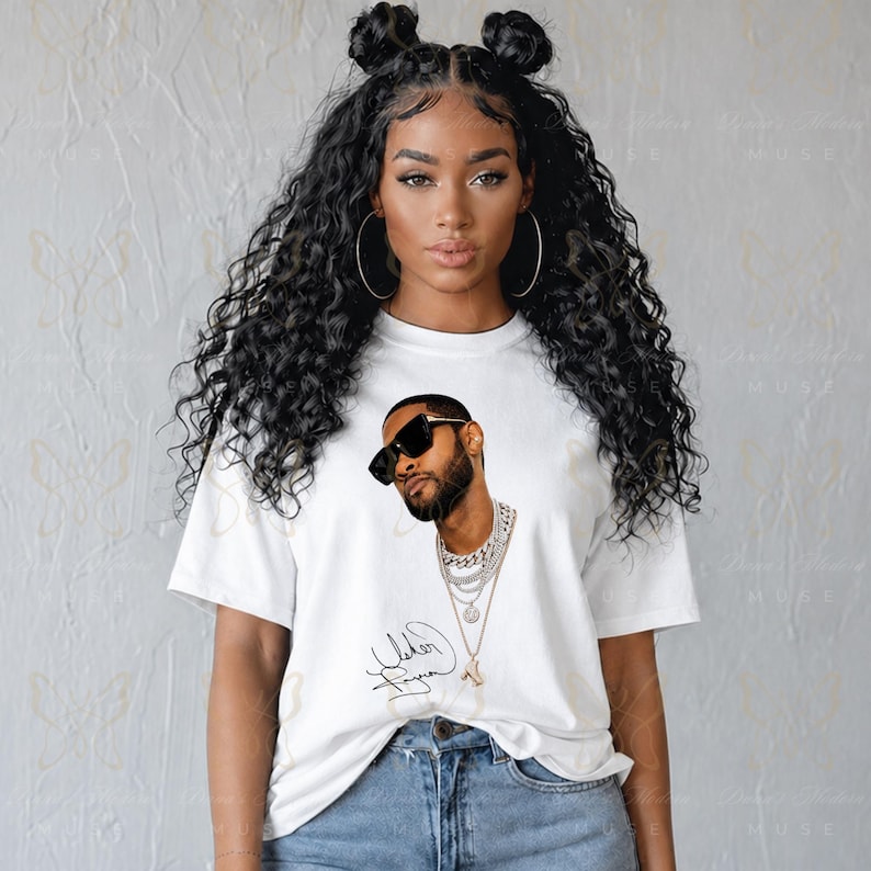 May include: A white short-sleeved t-shirt featuring a graphic print of a man with a beard wearing black sunglasses and layered silver chain necklaces. Below the graphic is a black cursive signature. The shirt is paired with blue denim jeans.
