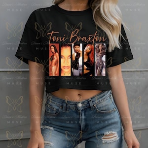 May include: Black crop top featuring the name "Toni Braxton" in a copper-colored script. The shirt displays a collage of images of Toni Braxton. The shirt is worn with blue jeans.