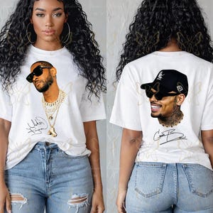 May include: A white short-sleeved t-shirt featuring a graphic print of a man wearing sunglasses and layered gold chains on the front, and a graphic print of a man wearing a black baseball cap and sunglasses on the back, with a signature below.