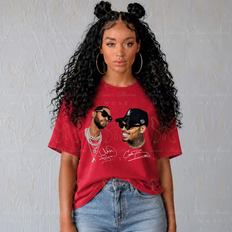 May include: A red short-sleeved t-shirt featuring a graphic print of two individuals wearing sunglasses and chains. The design includes white cursive signatures below each portrait. The shirt is paired with blue denim jeans.