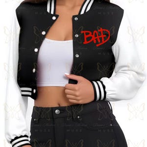May include: Black and white varsity jacket with the word "BAD" in red script on the chest. The jacket has white sleeves and black body with white stripes on the cuffs and collar. The jacket has white buttons.