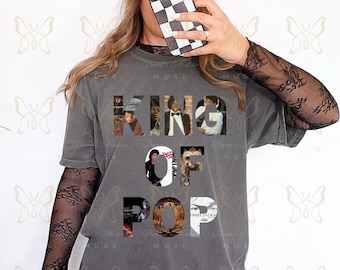 May include: Gray t-shirt with the words "KING OF POP" in a collage of images. The person is wearing a black and white checkered phone case and a white hat with the word "TIMELESS" on it. The person is also wearing a black lace sleeve shirt.