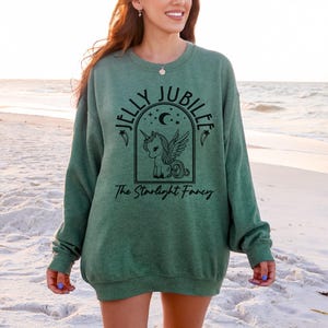 May include: Green sweatshirt with the text "JELLY JUBILEE" above a graphic of a winged unicorn inside an arch, with the text "The Starlight Fancy" below. The sweatshirt is a solid green color.