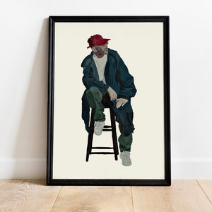 May include: Framed art print depicting a person seated on a stool. The person wears a red cap, a dark blue jacket, green trousers, and white trainers. The artwork is set against a cream background and framed in black.
