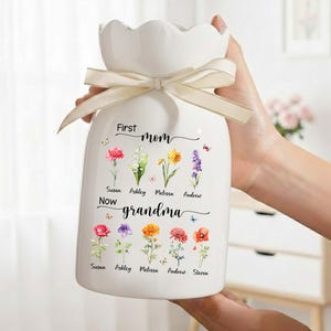 Pu&ograve; includere: Vaso in ceramica bianca con bordo smerlato e nastro color crema legato attorno al collo. Il vaso &egrave; decorato con illustrazioni floreali colorate e le parole "First mom, Now grandma". I nomi sono stampati sotto i fiori.