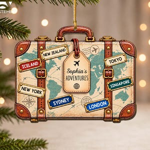 May include: A rectangular suitcase-shaped ornament featuring a vintage world map background. It includes a central luggage tag labeled 'Sophia's ADVENTURES' and various destination stickers: New Zealand, Iceland, New York, Tokyo, Singapore, Sydney, and London.