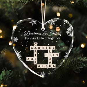 May include: A heart-shaped, clear glass ornament with the words "Brothers & Sisters Forever Linked Together." The names Gabriel, Lily, Zoe, and Aisha are displayed in a crossword-style arrangement. Snowflake designs are scattered across the ornament.