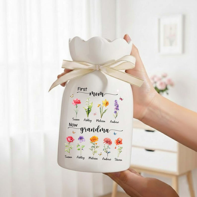 Pu&ograve; includere: Vaso in ceramica bianca con bordo smerlato e nastro color crema legato attorno al collo. Il vaso &egrave; decorato con illustrazioni floreali colorate e le parole "First mom, Now grandma". I nomi sono stampati sotto i fiori.