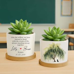 May include: Two white ceramic succulent planters with wooden saucers. One planter has text that reads "Like the willow...Lilly Bruno 9 years 15.05.2014". The other planter has a willow tree illustration.
