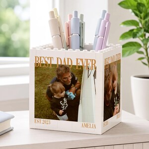 May include: White block-style pen holder with a photo of a father and child. The words "BEST DAD EVER" and "EST.2023" are printed in gold. Pastel pens are inside the holder.