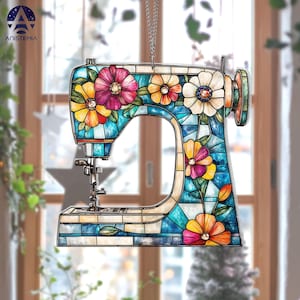 May include: A decorative sewing machine ornament with a stained glass design. The ornament features a blue body with colorful flowers in shades of pink, yellow, and orange. It hangs from a silver chain, perfect for a craft room or sewing enthusiast.