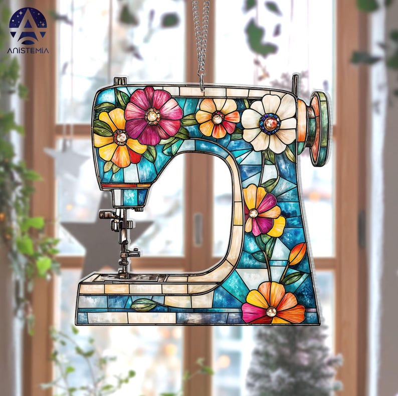 May include: A decorative sewing machine ornament with a stained glass design. The ornament features a blue body with colorful flowers in shades of pink, yellow, and orange. It hangs from a silver chain, perfect for a craft room or sewing enthusiast.