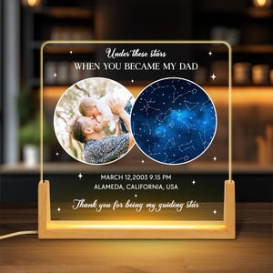 May include: A personalized LED night light with a wooden base. The light features two circular images: a photo of a father and child, and a starry night sky. Text includes "Under these stars, When you became my Dad," and a date and location.