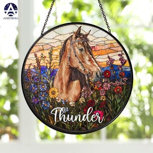 Pode incluir: Um apanhador de sol circular em vitral com um cavalo castanho com r&eacute;deas, rodeado de flores silvestres coloridas e uma paisagem ao p&ocirc;r do sol. A palavra Thunder est&aacute; escrita em letra branca na parte inferior da moldura.