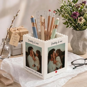 May include: A white block-style pen holder with the words "Daddy & me" and a photo of a father and child. The holder contains pens, pencils, and a ruler. The text "To the greatest dad, with all my love" is printed on the front.