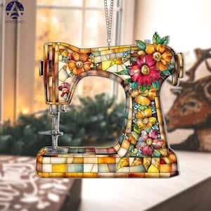 May include: A decorative sewing machine ornament with a stained-glass effect. The ornament features a colorful floral design with red, orange, and yellow flowers. The sewing machine is suspended by a silver chain. The word "ANISTEMIA" is printed on the top left.