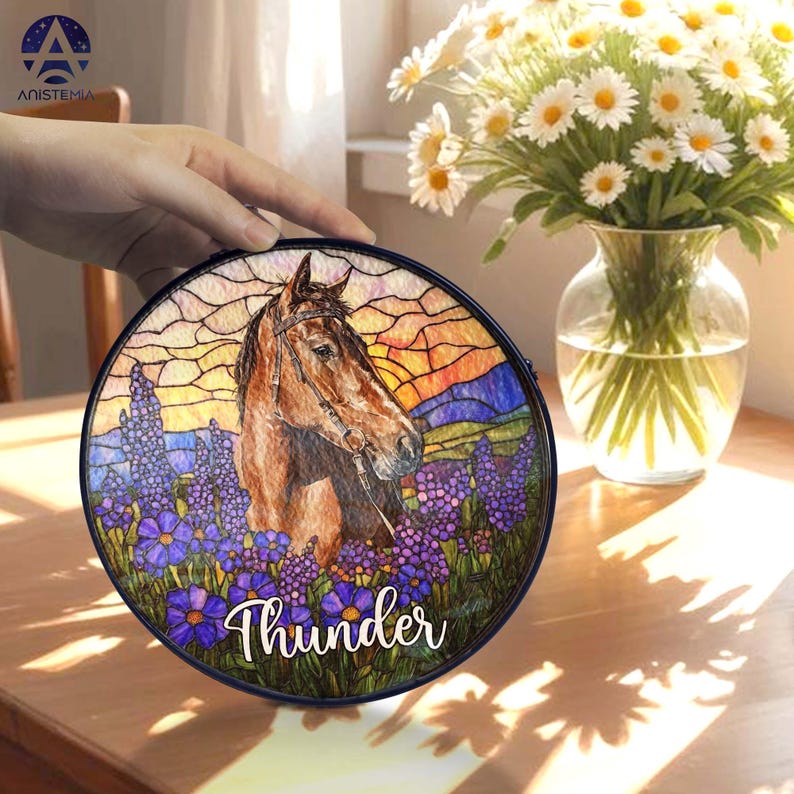 Pode incluir: Uma placa decorativa circular com uma ilustra&ccedil;&atilde;o em estilo vitral de um cavalo castanho num campo de flores roxas sob um c&eacute;u ao p&ocirc;r do sol. O nome Thunder est&aacute; escrito em letra cursiva branca na parte inferior.