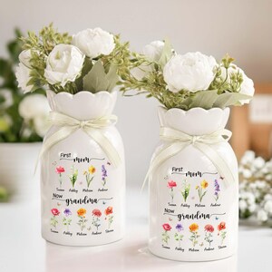 Pu&ograve; includere: Due vasi in ceramica bianca con composizioni floreali. Ogni vaso ha un bordo smerlato, un nastro color crema e un motivo floreale con le parole "First Mom Now Grandma" e nomi. I vasi sono pieni di fiori bianchi.