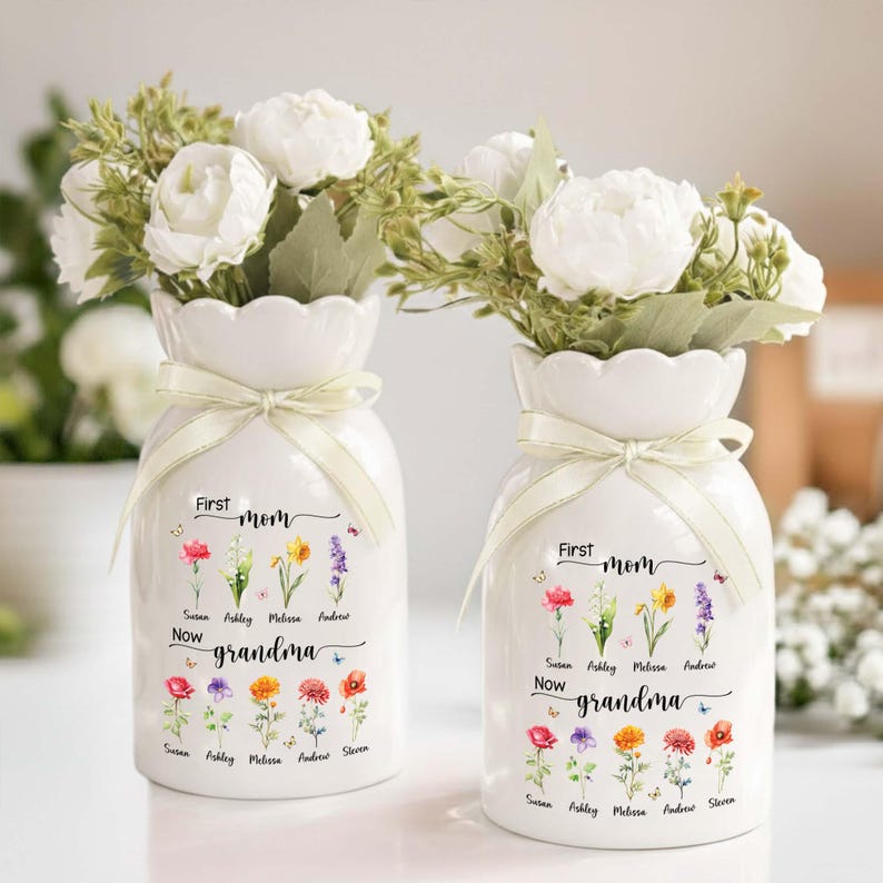 Pu&ograve; includere: Due vasi in ceramica bianca con composizioni floreali. Ogni vaso ha un bordo smerlato, un nastro color crema e un motivo floreale con le parole "First Mom Now Grandma" e nomi. I vasi sono pieni di fiori bianchi.