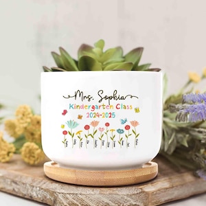May include: White ceramic planter with a bamboo base. The planter has a floral design with butterflies and the text "Mrs. Sophia Kindergarten Class 2024-2025" and a list of names.