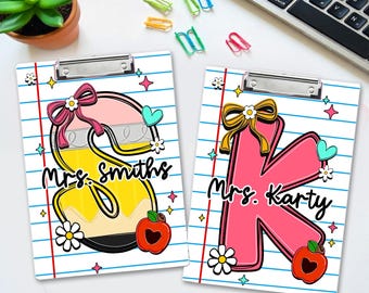 Könnte beinhalten: Zwei Klemmbretter mit Liniendesign. Eines zeigt einen großen Buchstaben "S" mit einem Bleistift-Design, dem Text "Mrs. Smiths" und einem Apfel. Das andere hat ein "K" mit dem Text "Mrs. Karty" und einem Apfel.