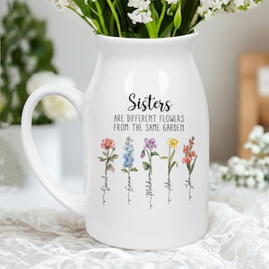 May include: White ceramic pitcher with a handle, filled with white flowers. The pitcher has the text "Sisters are different flowers from the same garden" and features floral illustrations with names below.